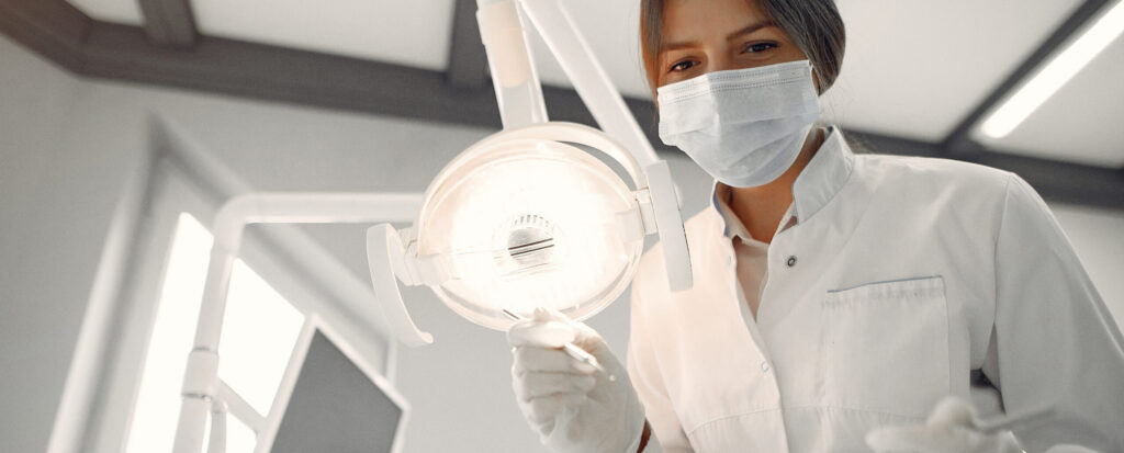 Zahnärztin mit Maske prüft Licht im Behandlungsraum.