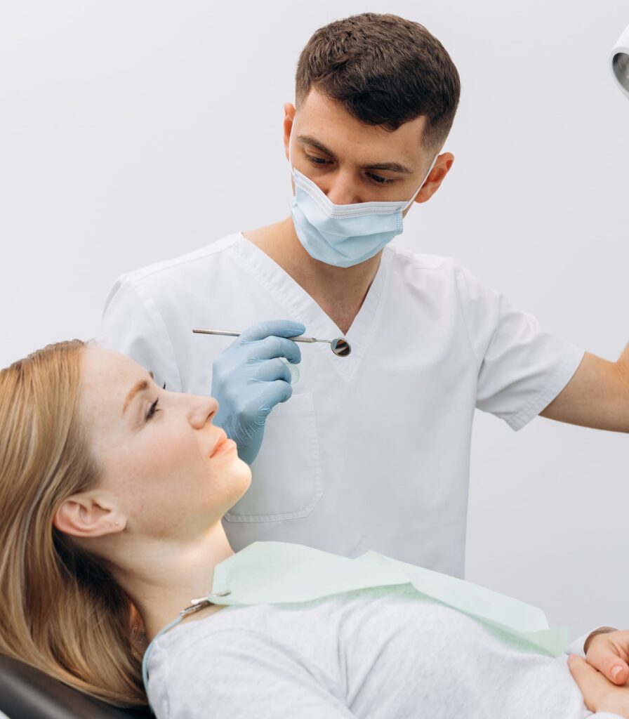 Zahnarzt untersucht Patientin mit Spiegel im Behandlungsraum.