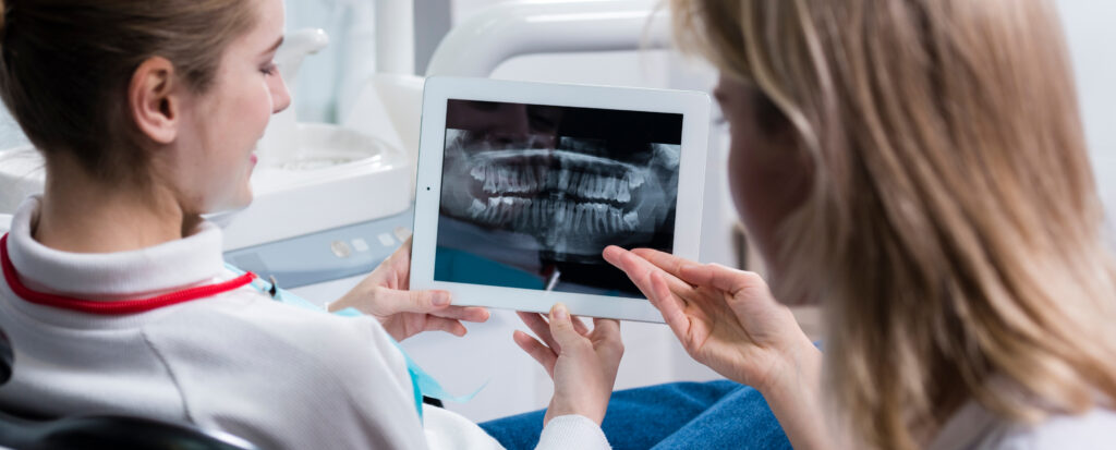 Zahnärztin zeigt Patientin Röntgenbild auf Tablet.