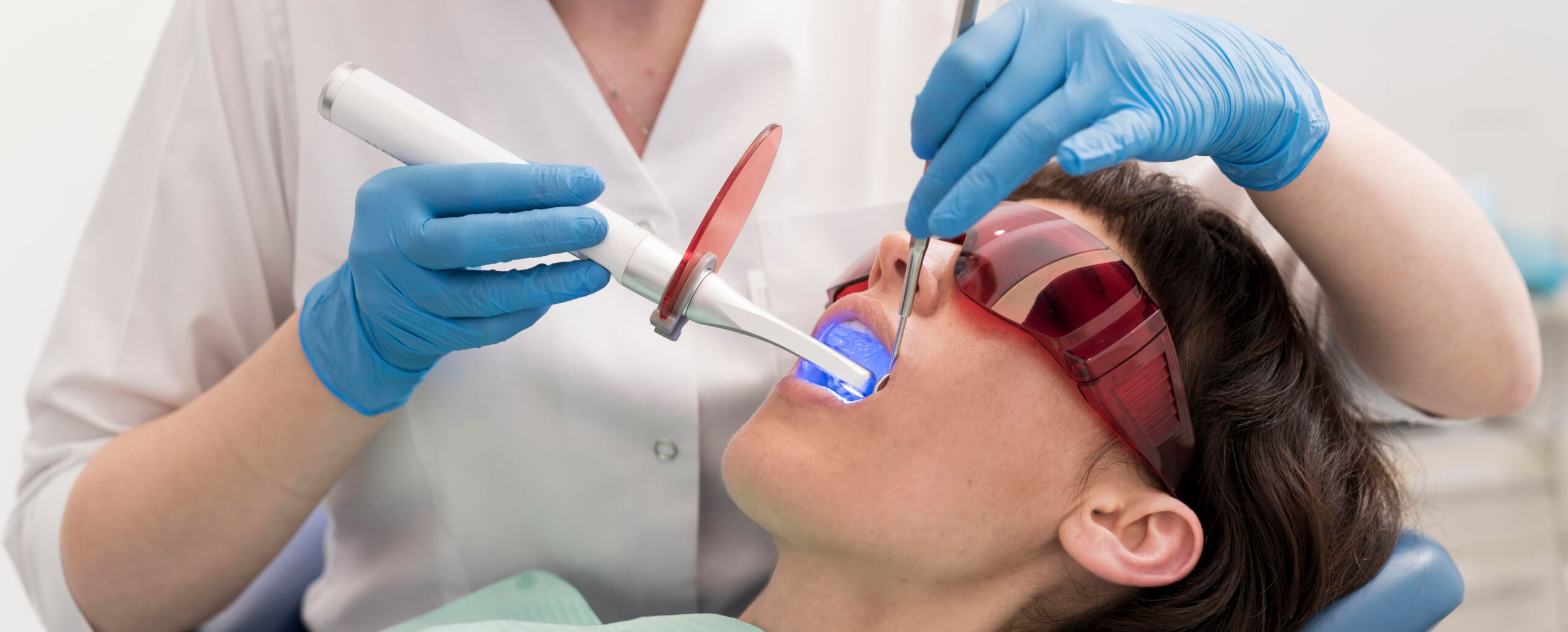 Zahnbehandlung mit Blaulicht bei Zahnarzt, Patient trägt Schutzbrille.
