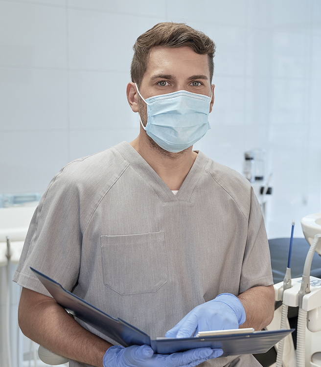 Zahnarzt mit Maske in moderner Praxis hält Patientenakte.