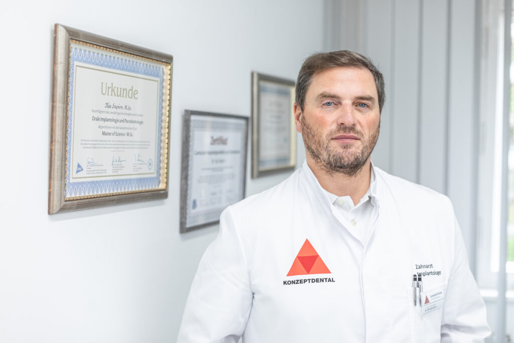 Zahnarzt vor Zertifikaten, Praxisraum, KonzeptDental, implantologische Expertise.