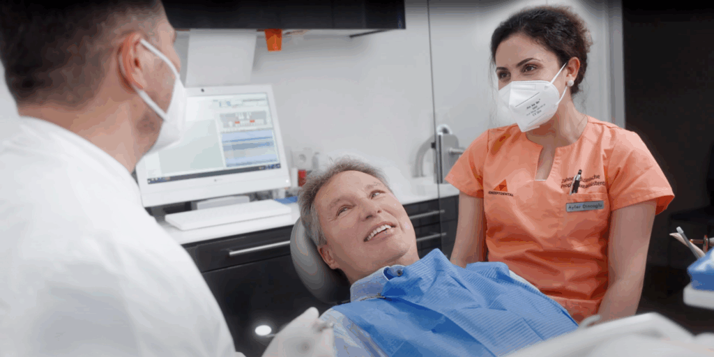 Zahnarzt im Gespräch mit einem lächelnden Patienten und Assistentin in der Praxis.